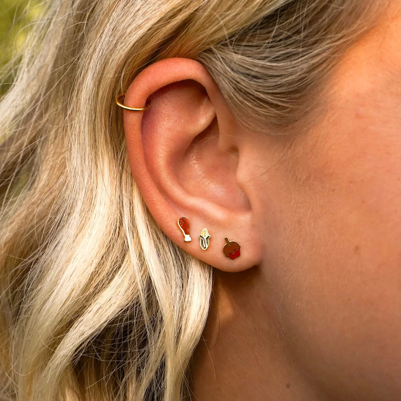 Close-up of a person's ear with multiple earrings against a blurred natural background