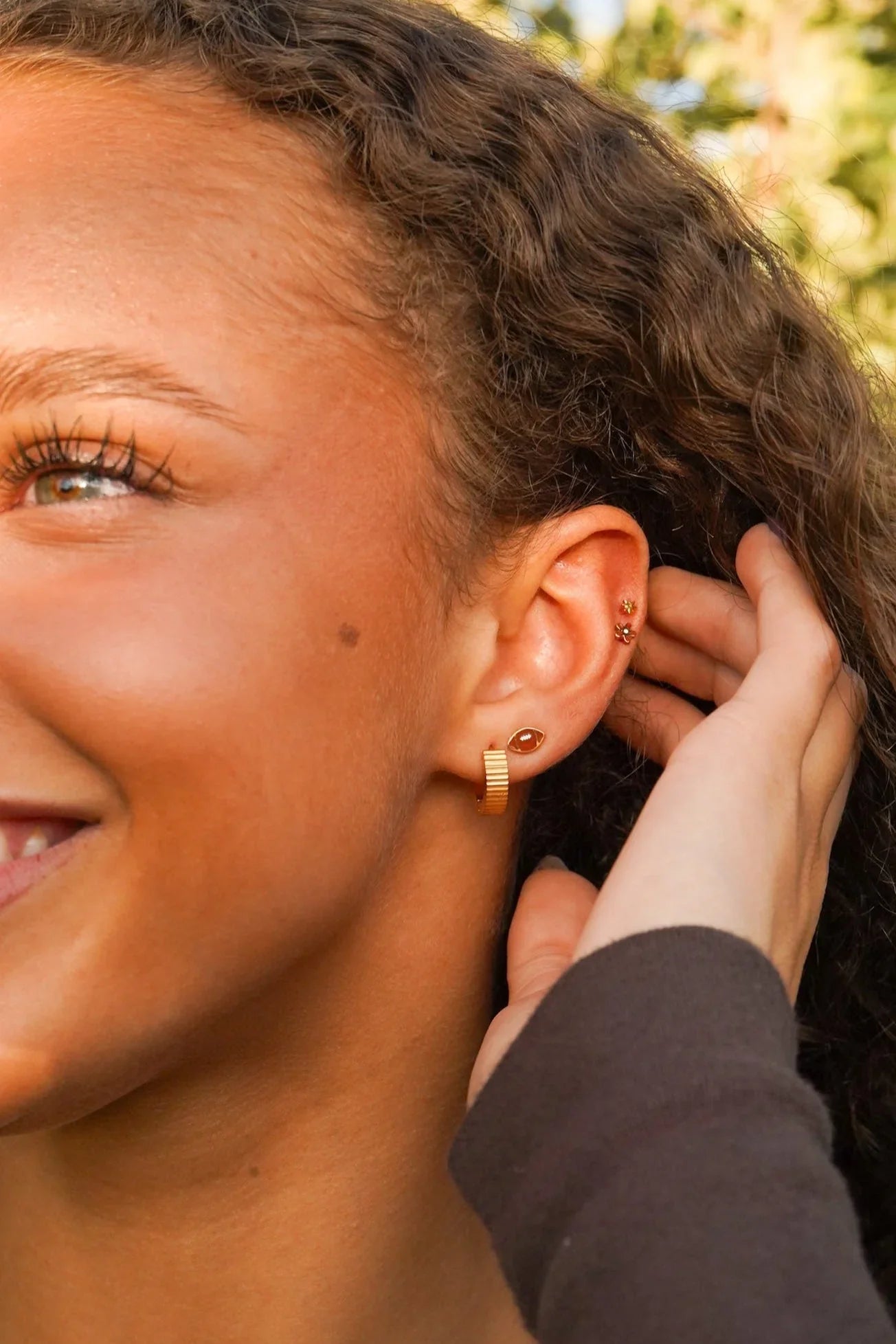 Close-up of a person wearing gold earrings with a blurred natural background