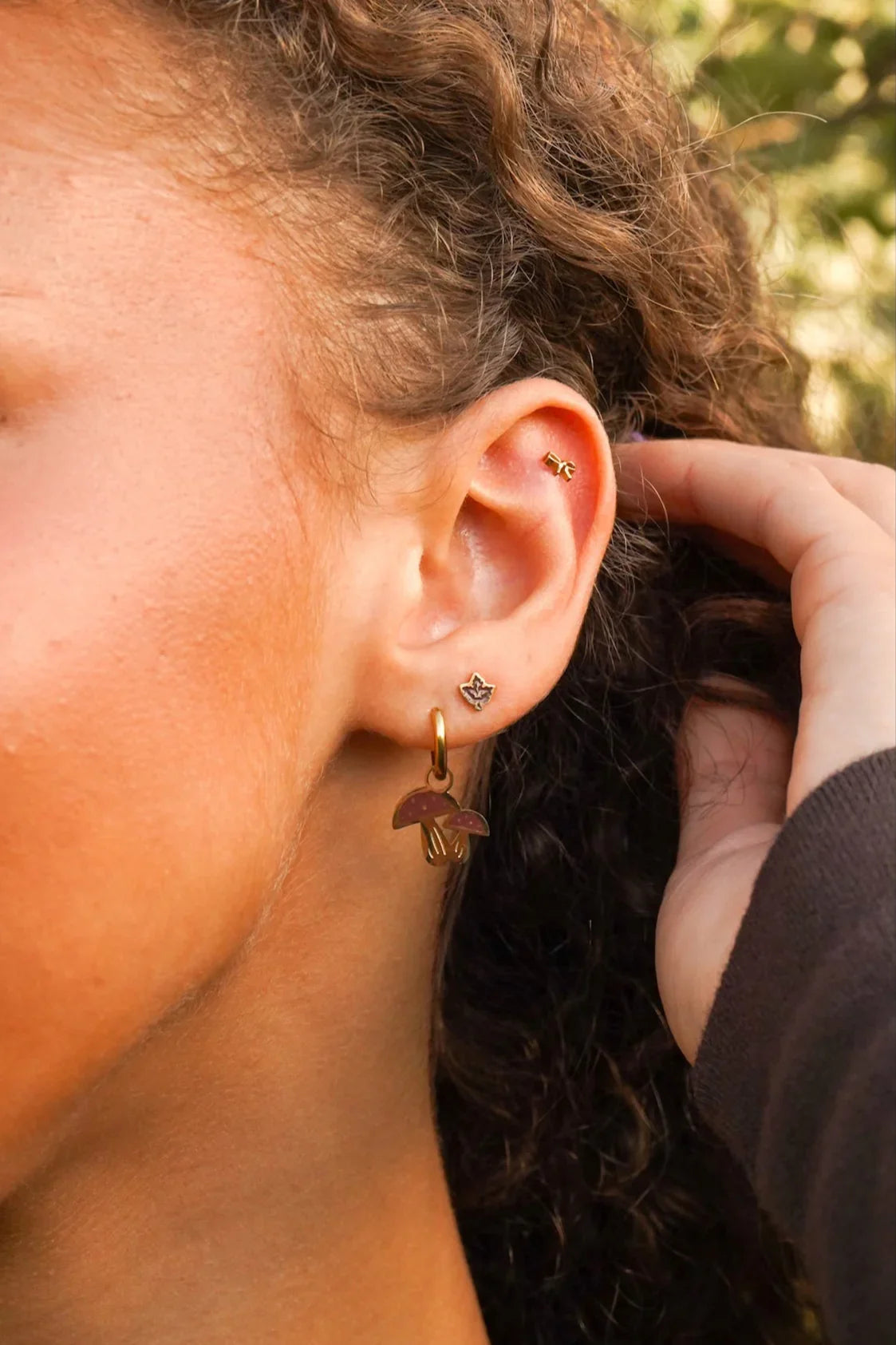 Close-up of a person wearing a brown maple leaf stud earring with a blurred background