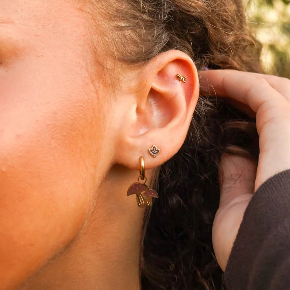 Close-up of a person wearing a brown maple leaf stud earring with a blurred background