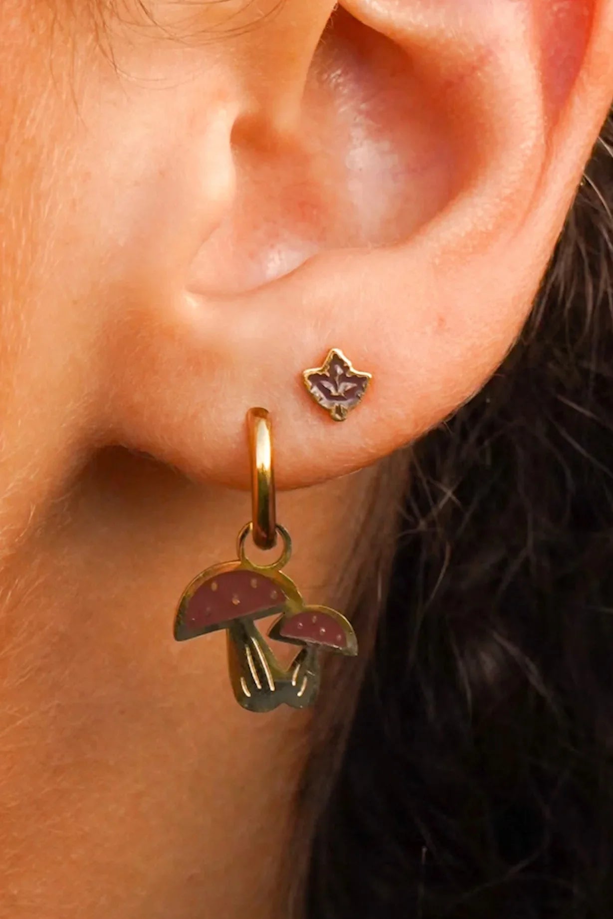 Close-up of an ear wearing a gold earring with mushroom charms.