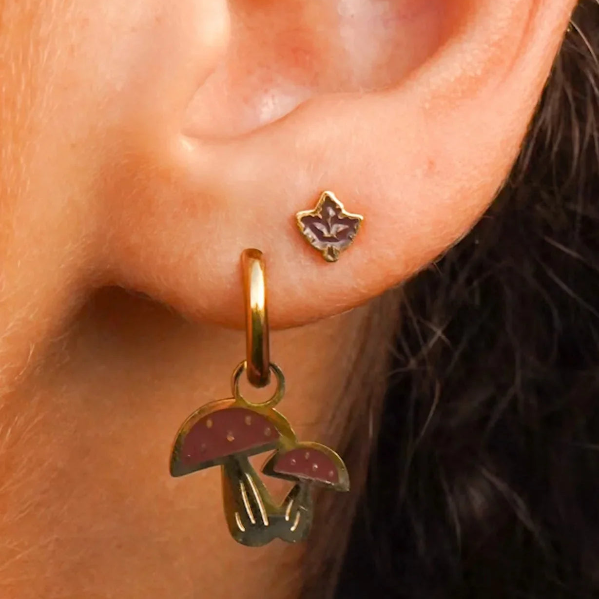 Close-up of an ear wearing a gold earring with mushroom charms.