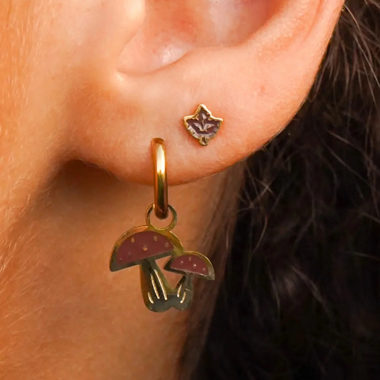 Close-up of an ear wearing a gold earring with mushroom charms.