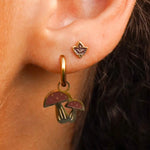 Close-up of an ear wearing a gold earring with mushroom charms.