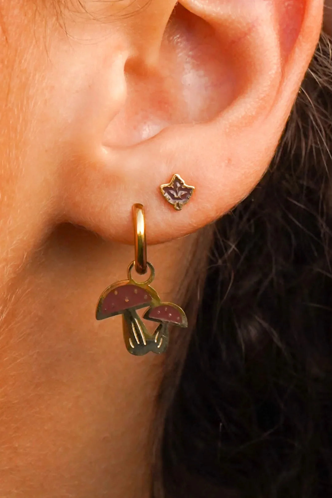 Close-up of an ear wearing a gold earring with mushroom charms.