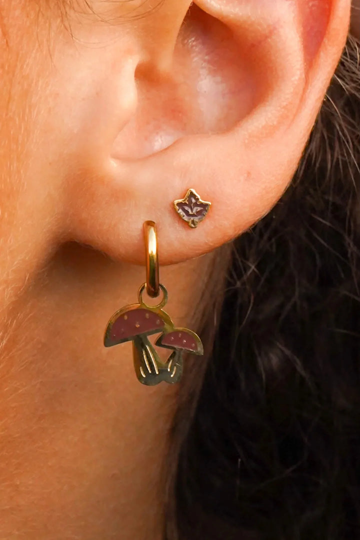 Close-up of an ear wearing a gold earring with mushroom charms.