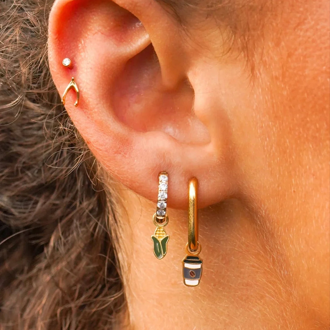 Close-up of an ear wearing gold hoop earrings with charms on them and a blurred background