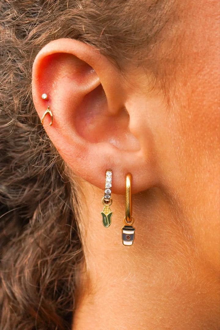 Close-up of an ear wearing gold hoop earrings with charms on them and a blurred background