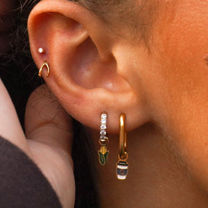 Close-up of an ear wearing gold hoop earrings with small charms.