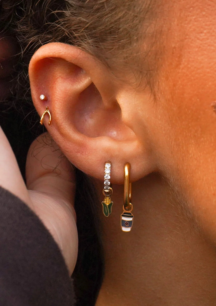 Close-up of an ear wearing gold hoop earrings with small charms.