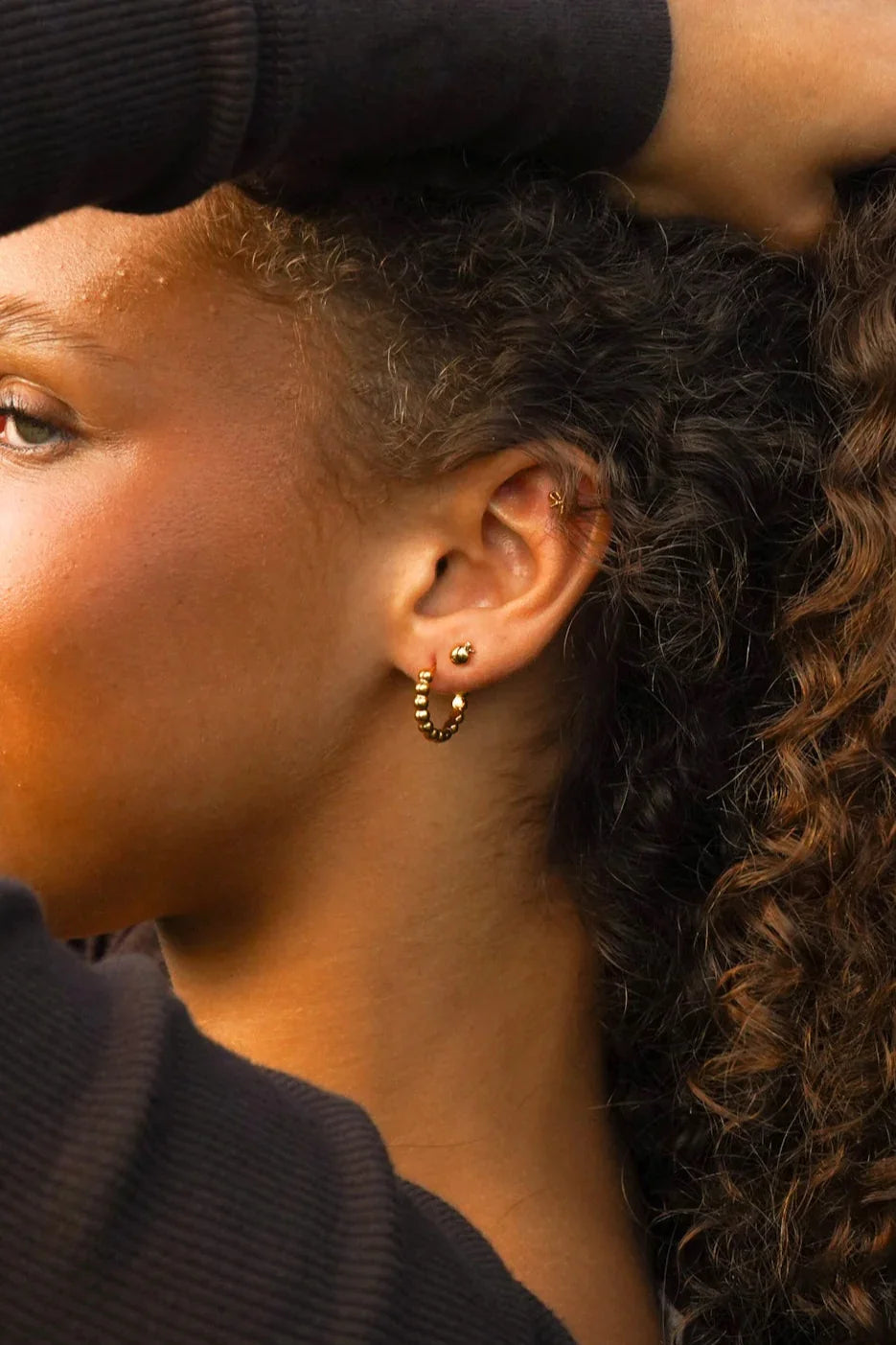 Close-up of an pearson wearing gold hoop earring and a 3D apple-shaped stud earring