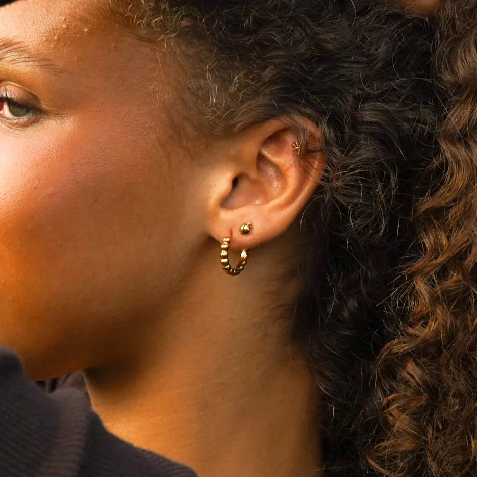 Close-up of an pearson wearing gold hoop earring and a 3D apple-shaped stud earring