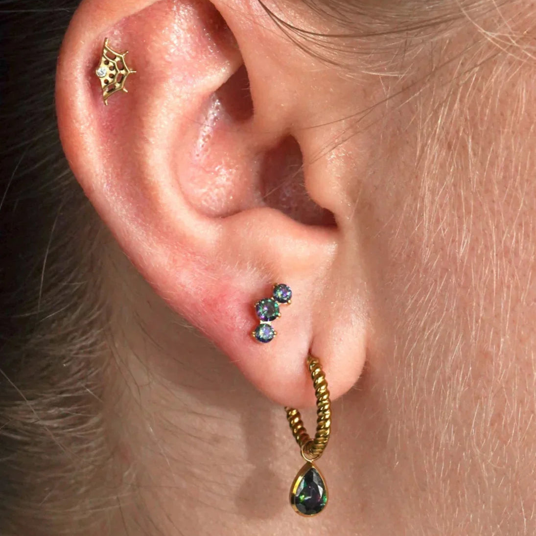 Close-up of an ear with gold and green earrings.
