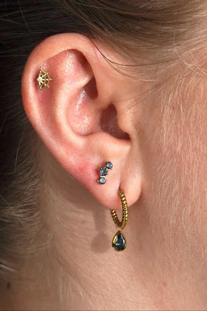 Close-up of an ear with gold and green earrings.