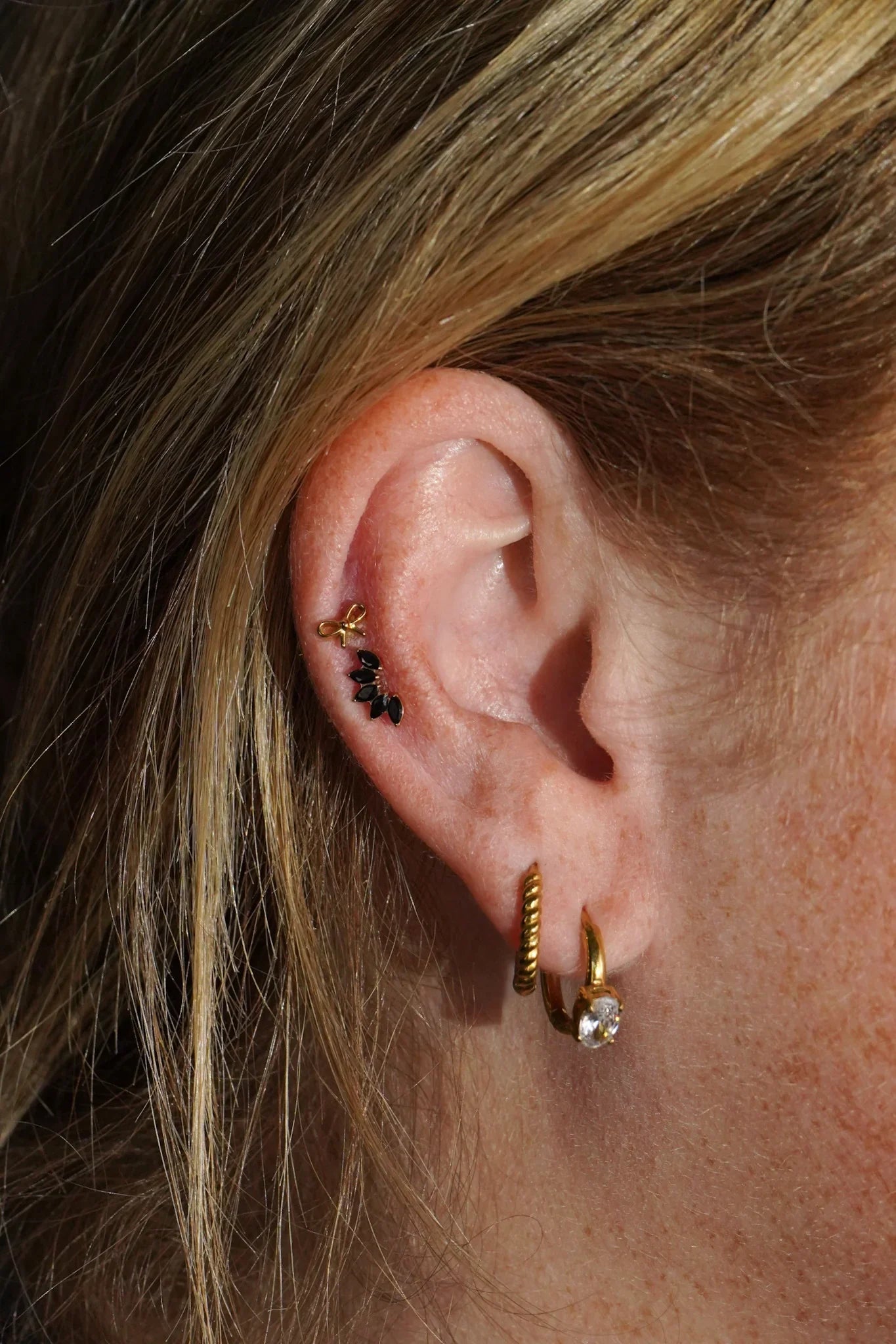 Close-up of an ear with double gold hoop earrings, and black and gold studs.