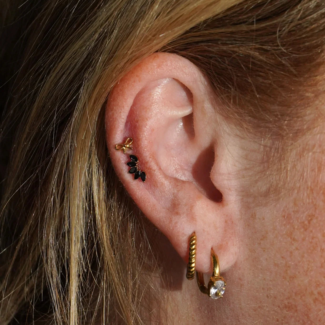 Close-up of an ear with double gold hoop earrings, and black and gold studs.