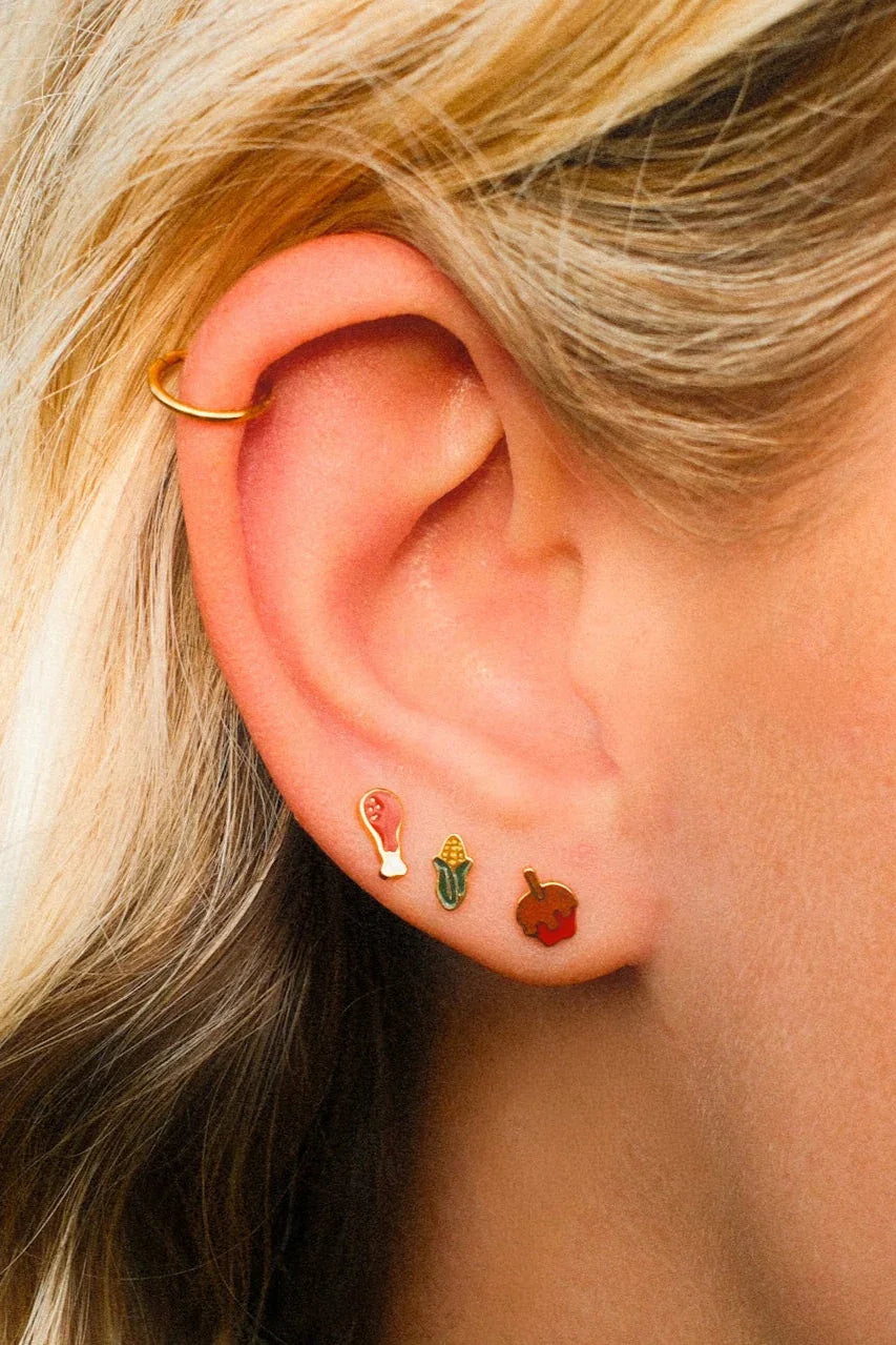 Close-up of an ear with gold hoop earrings and colorful studs.