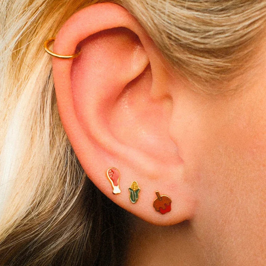 Close-up of an ear with gold hoop earrings and colorful studs.