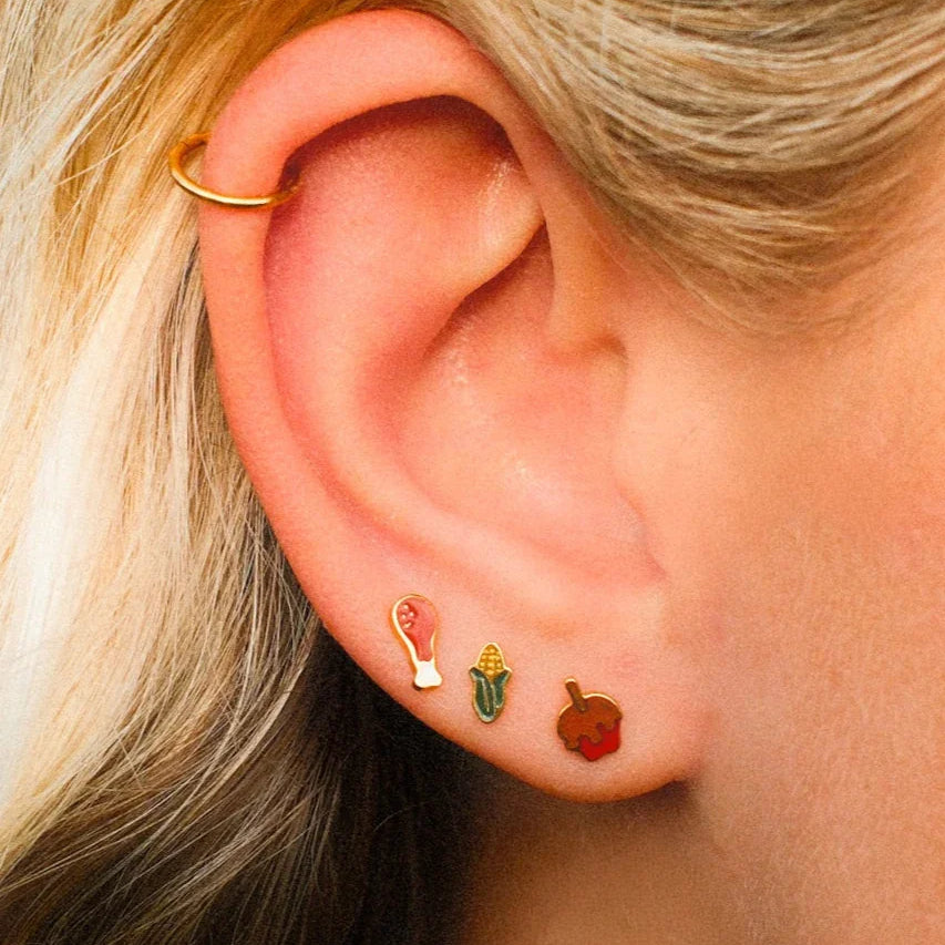 Close-up of an ear with gold hoop earrings and colorful studs.