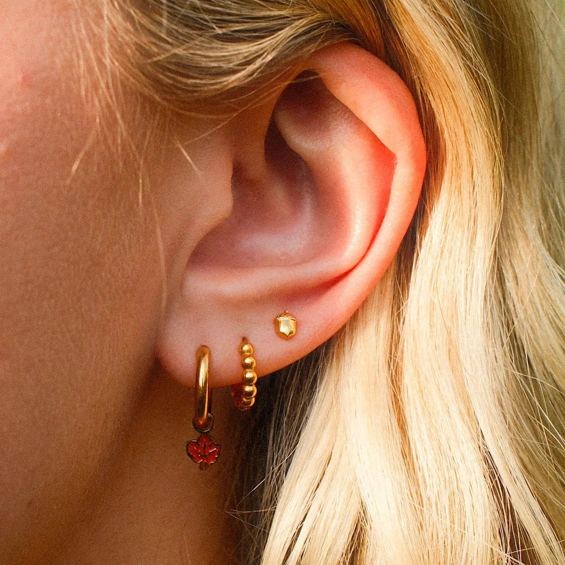 Close-up of an ear with gold hoop earrings and a red earring.