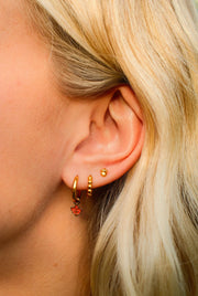 Close-up of an ear wearing gold hoop earrings with red gemstones.