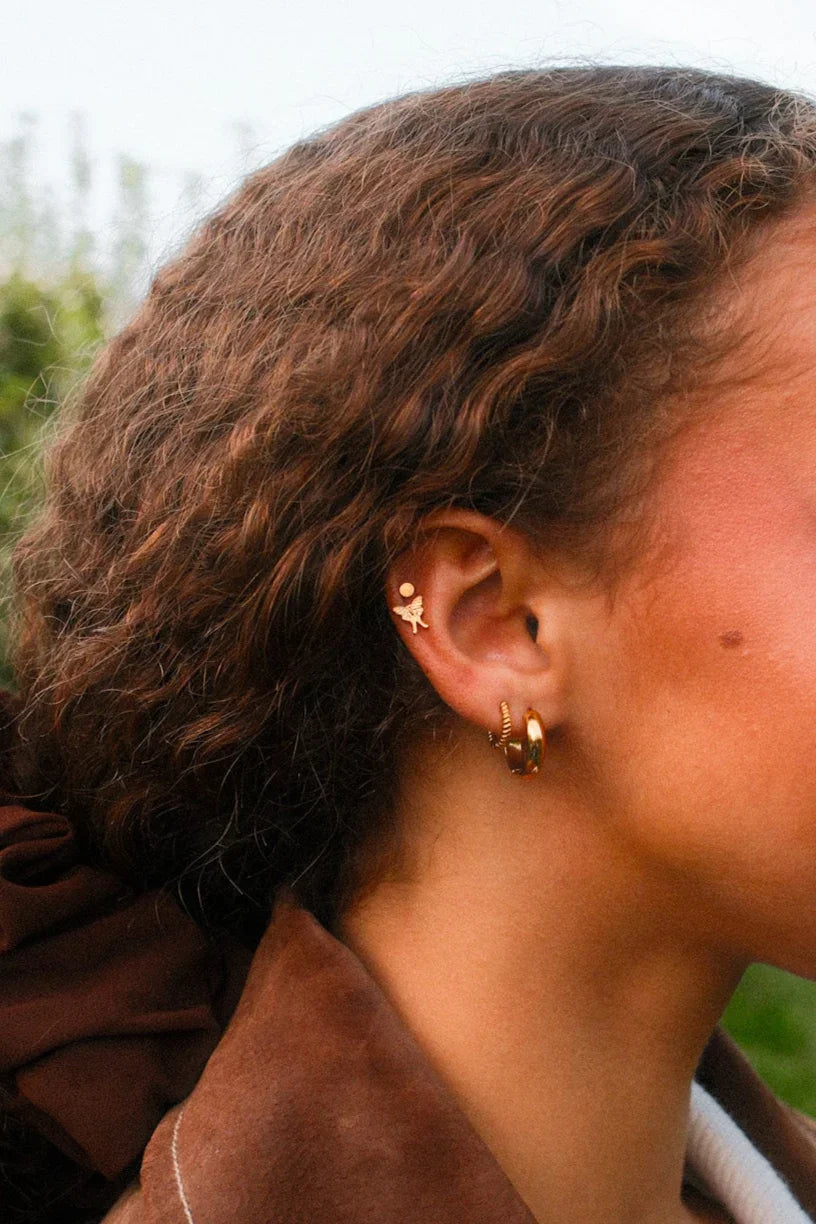Woman with curly hair and a brown jacket outdoors in an apple orchard