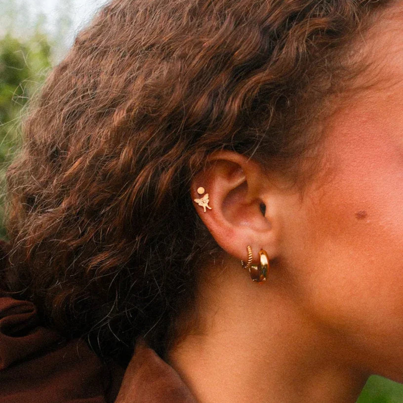 Woman with curly hair and a brown jacket outdoors in an apple orchard