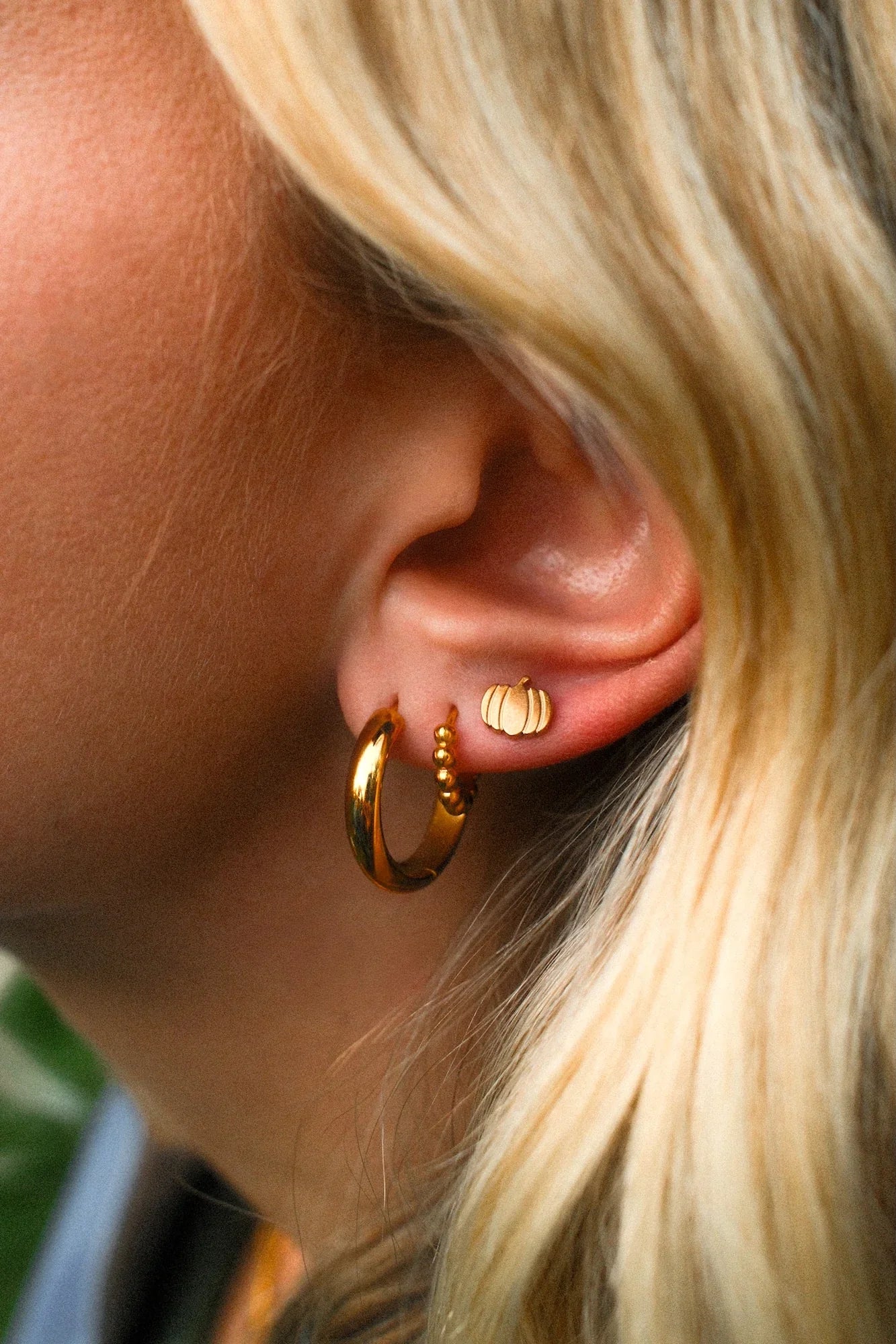 Close-up of a person wearing gold hoop earrings with a blurred background