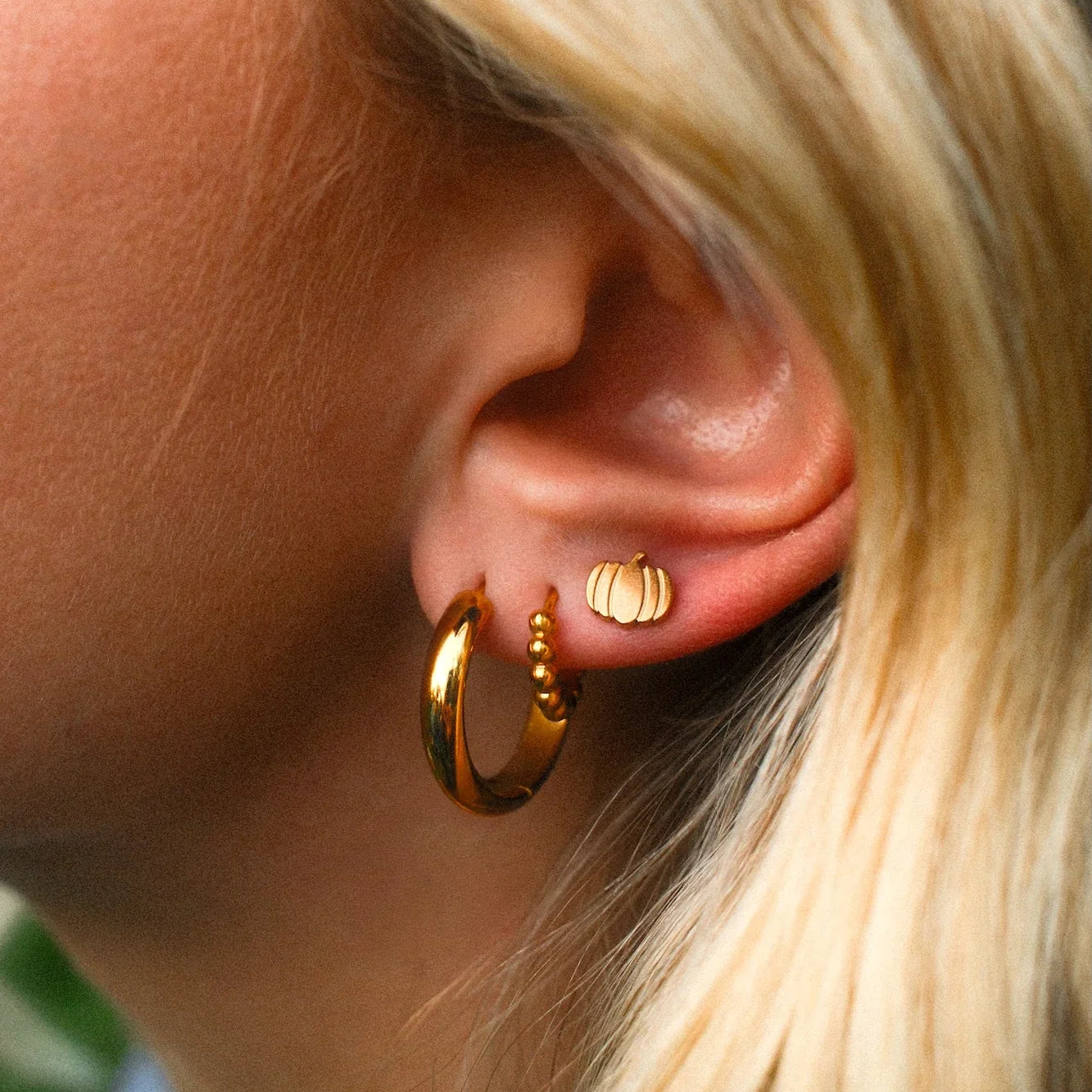 Close-up of a person wearing gold hoop earrings with a blurred background