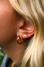 Close-up of a person wearing gold hoop earrings with a blurred background