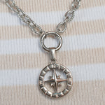 A silver compass pendant necklace resting on a pink and cream striped knit sweater.