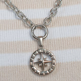 A silver compass pendant necklace resting on a pink and cream striped knit sweater.