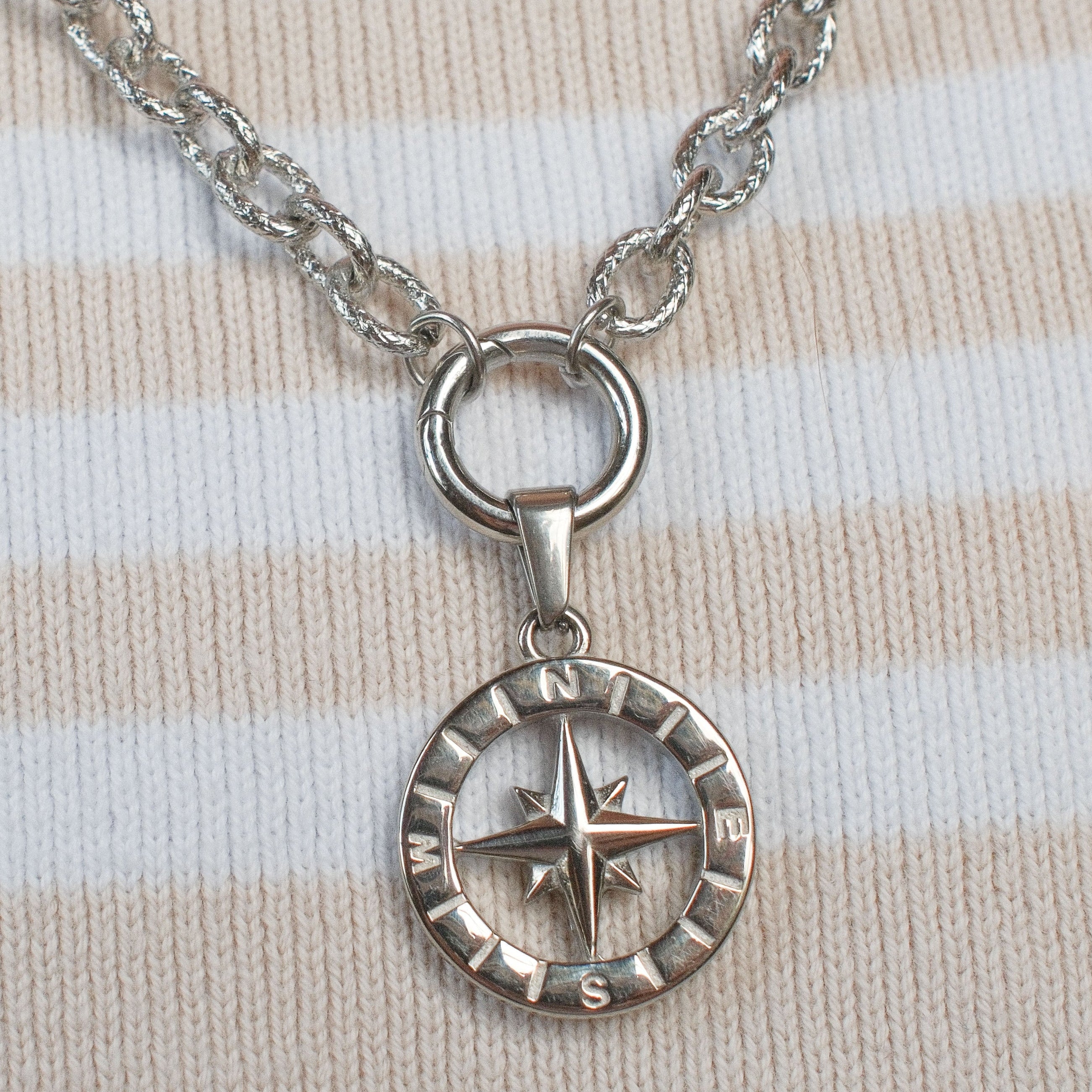 A silver compass pendant necklace resting on a pink and cream striped knit sweater.