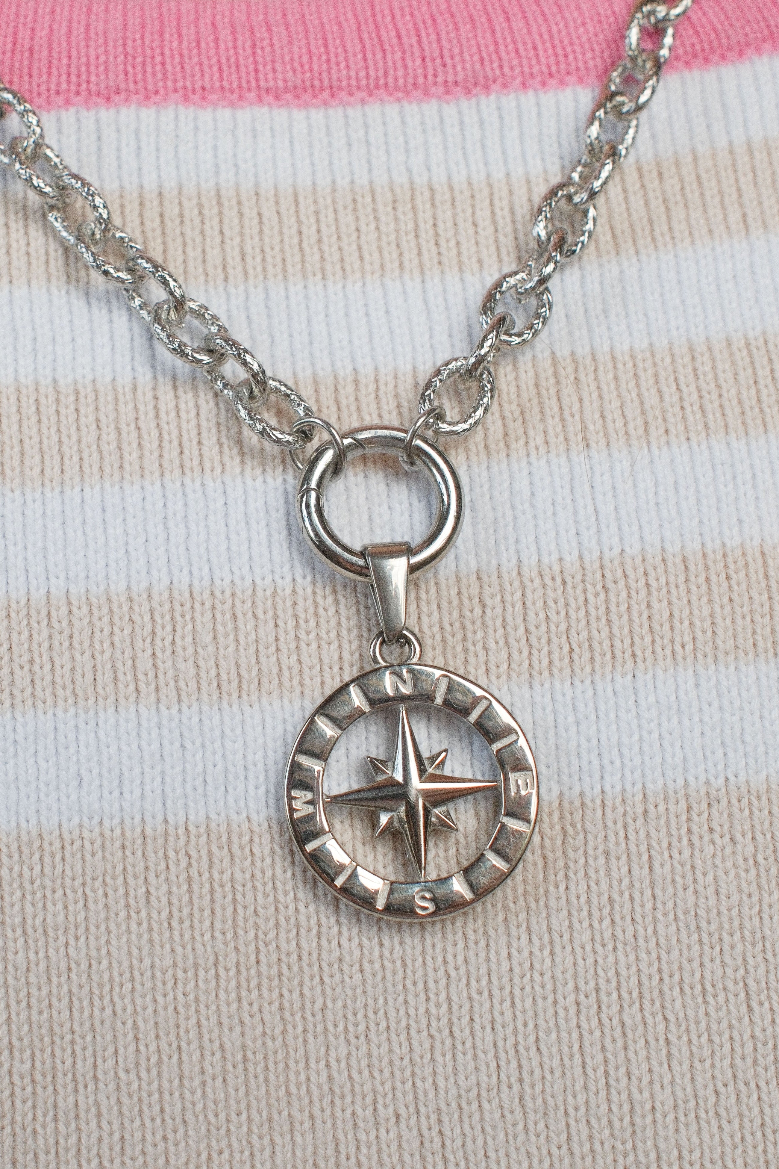 A silver compass pendant necklace resting on a pink and cream striped knit sweater.
