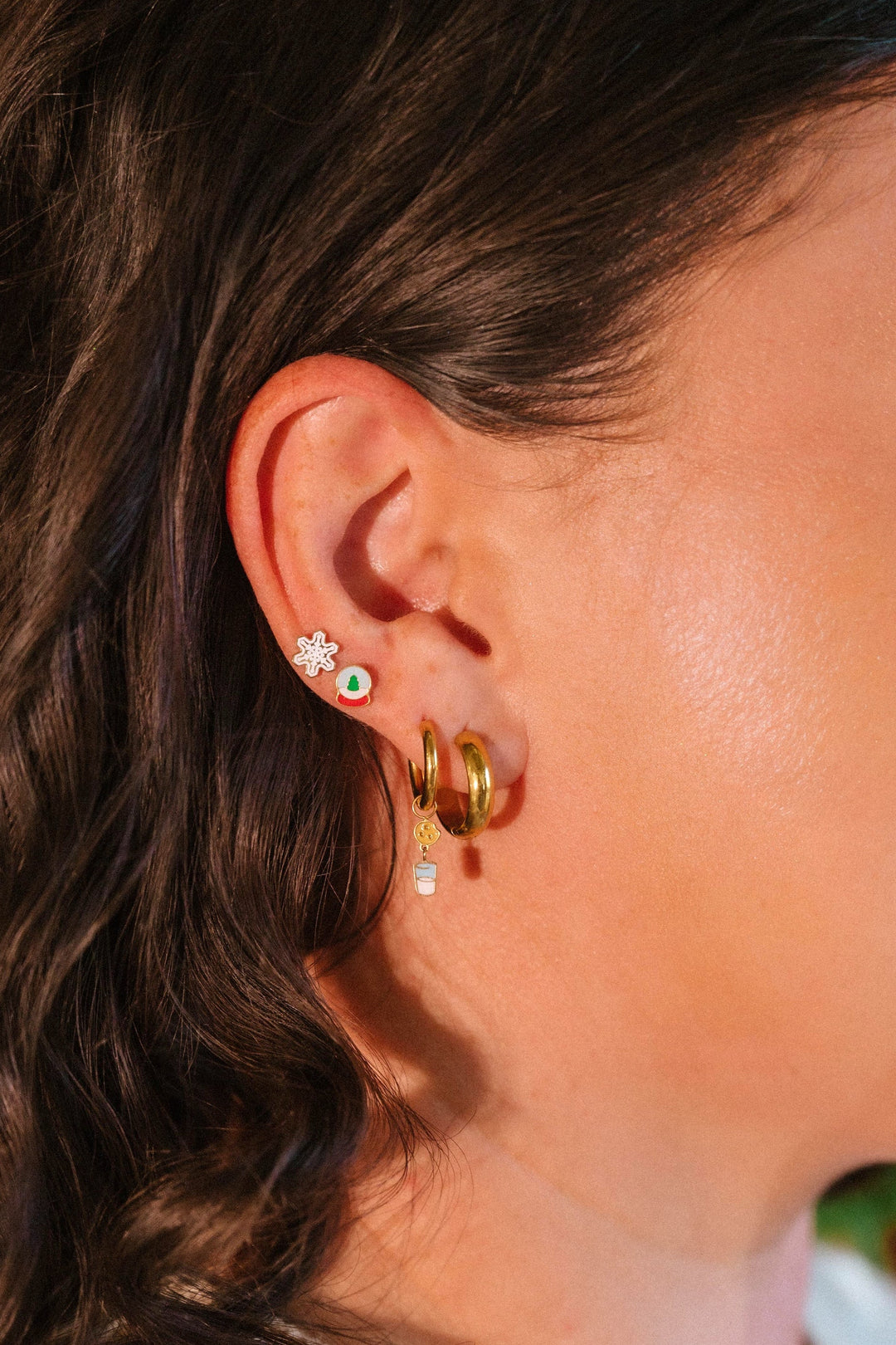 Close-up of a person's ear wearing gold hoop earrings with green gemstones.