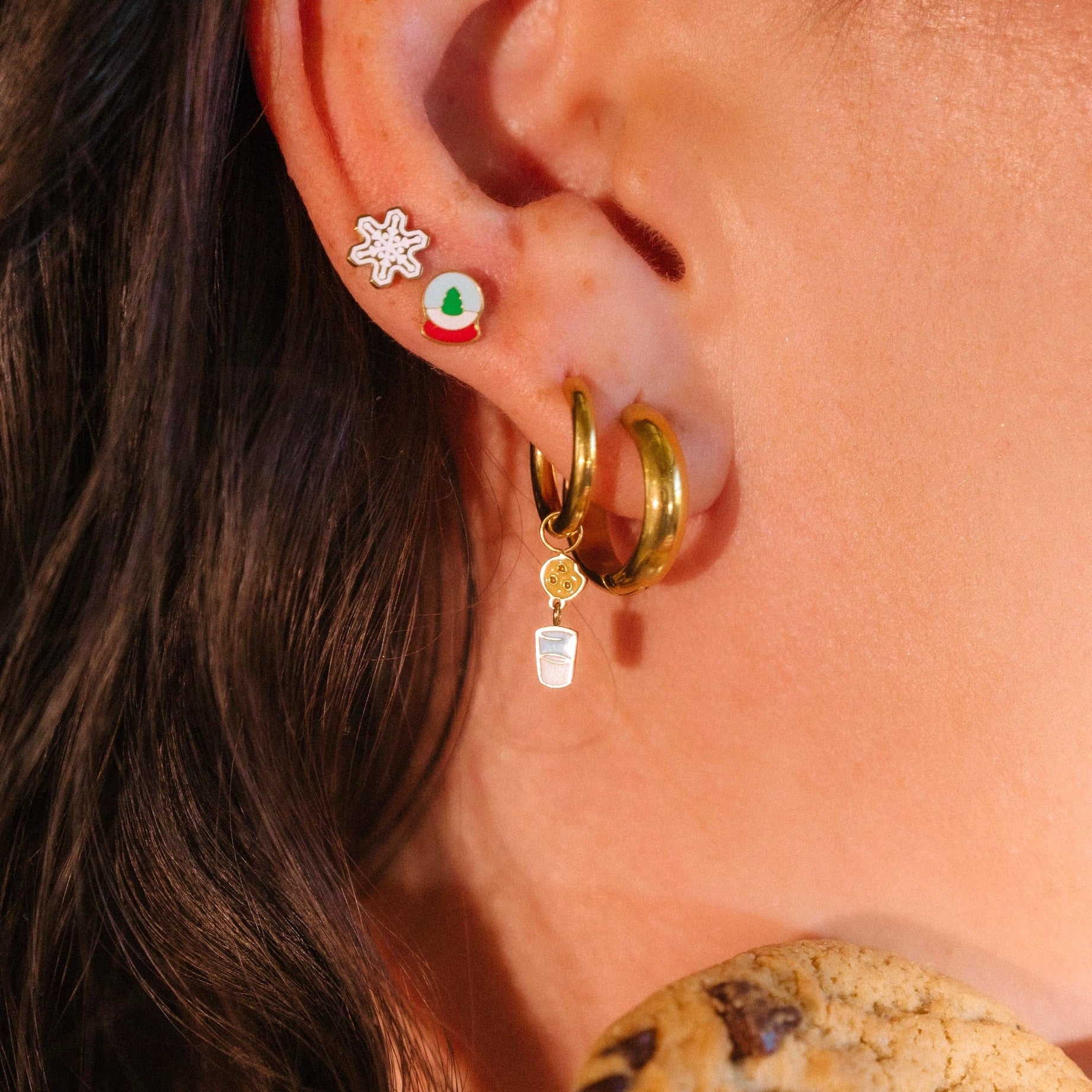 Close-up of an ear with gold hoop earrings and a cookie in the foreground