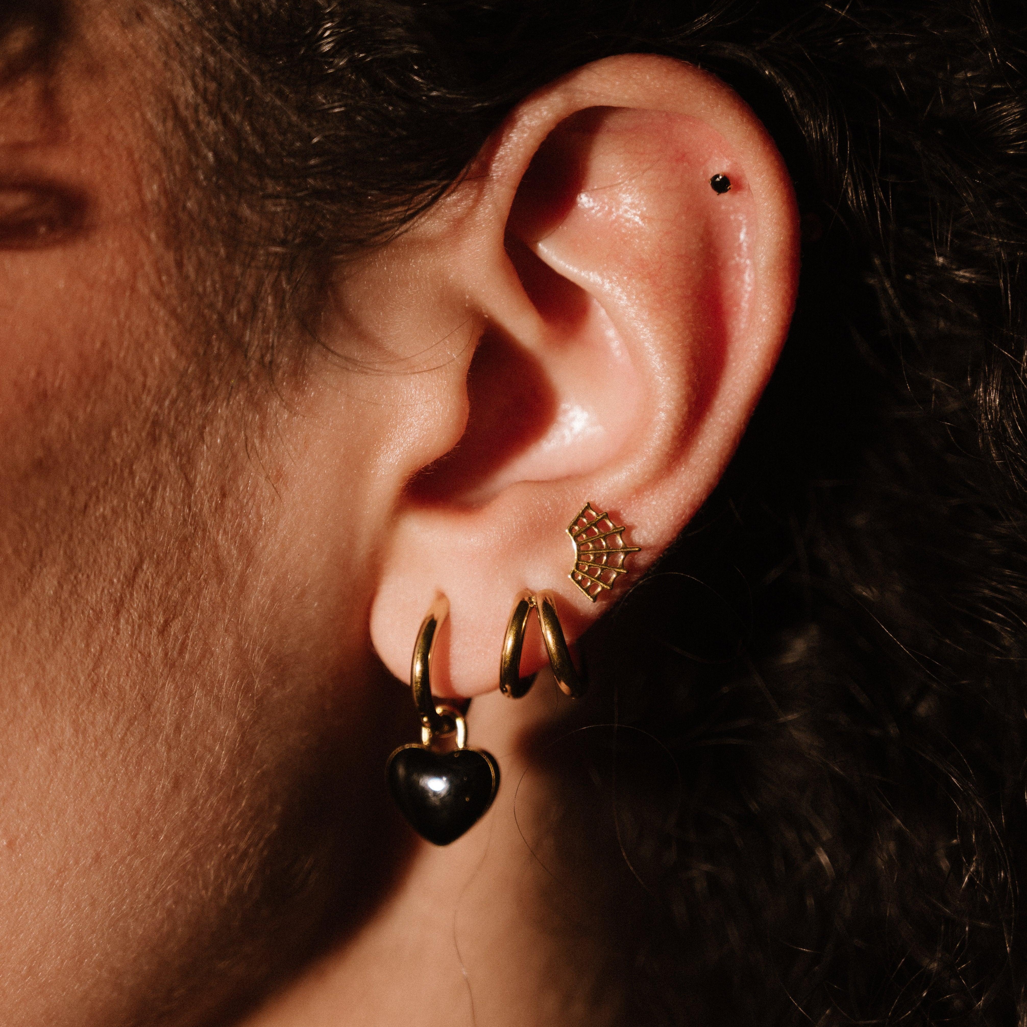 Close-up of an ear with gold and black earrings against a dark background