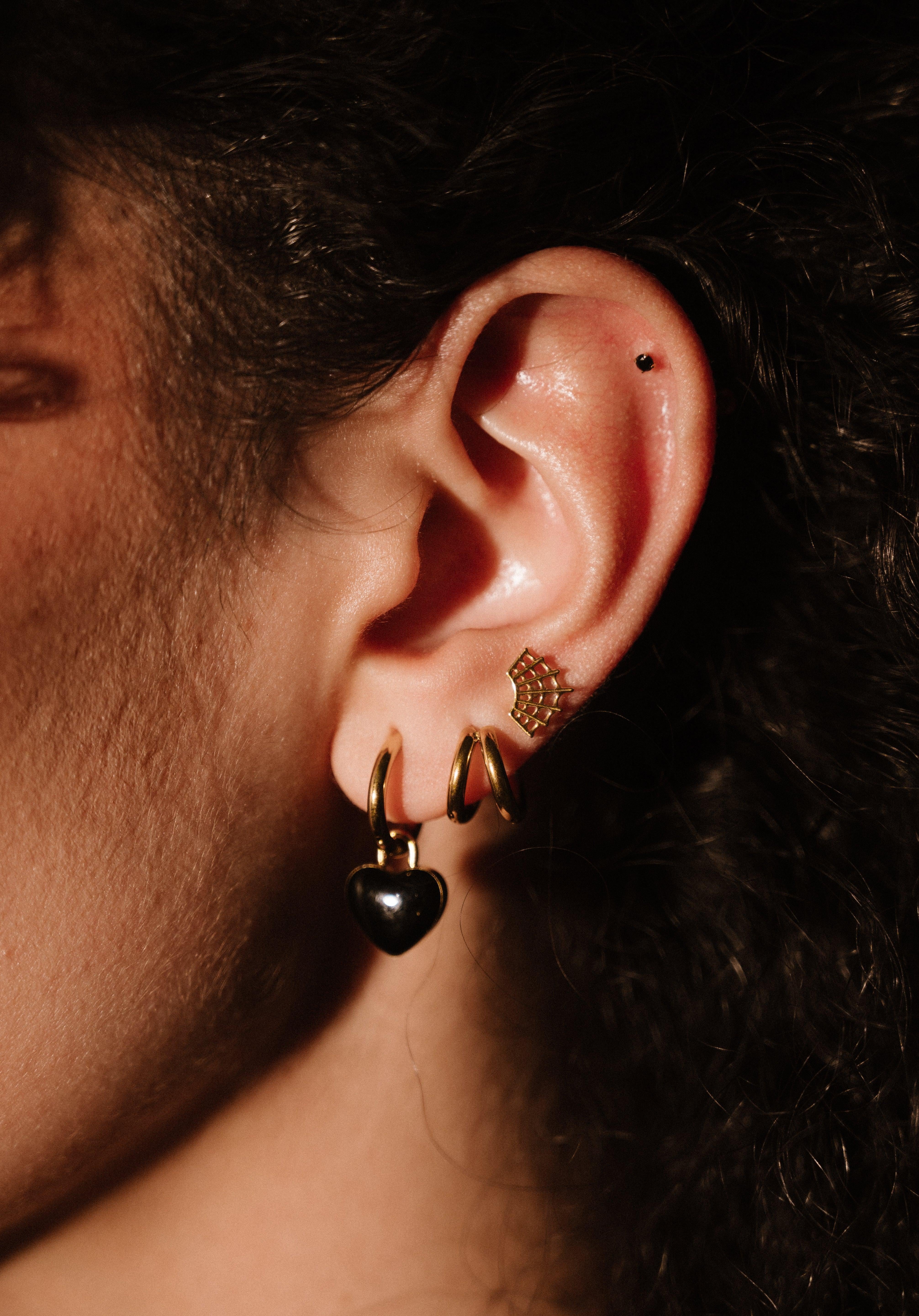 Close-up of an ear with gold and black earrings against a dark background