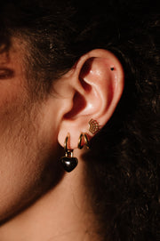 Close-up of an ear with gold and black earrings against a dark background