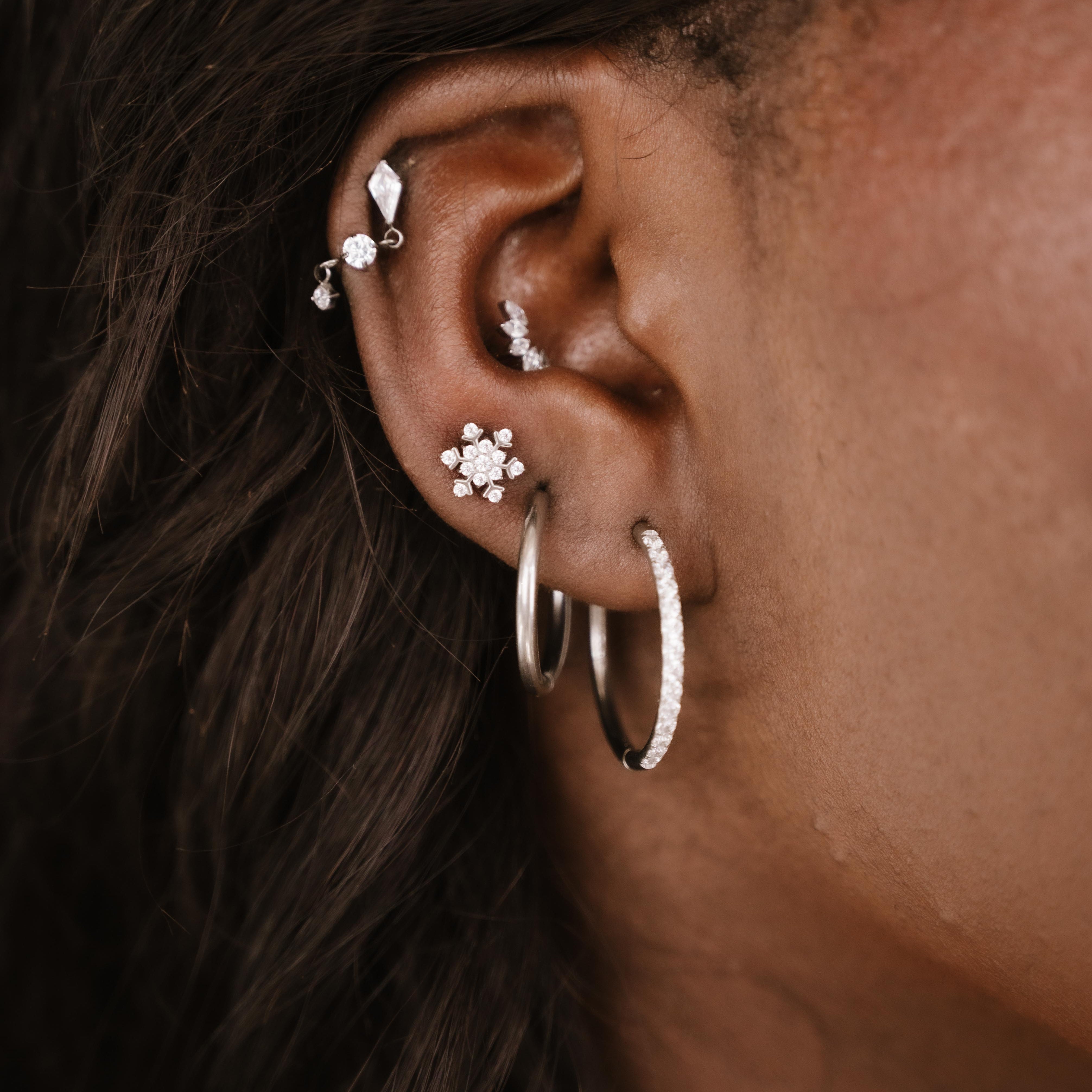 Close-up of an ear with multiple silver and clear zirconia earrings 