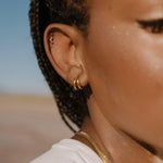 Close-up of a person wearing double gold hoop earrings with a blurred natural landscape in the background