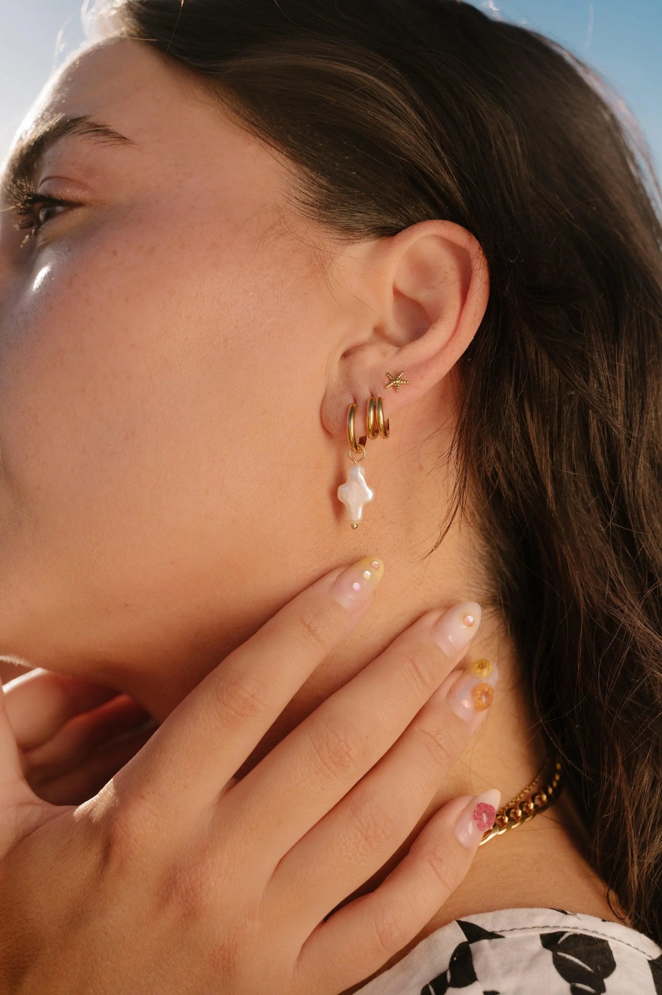 Close-up of a person wearing multiple gold hoop earrings with a blurred background