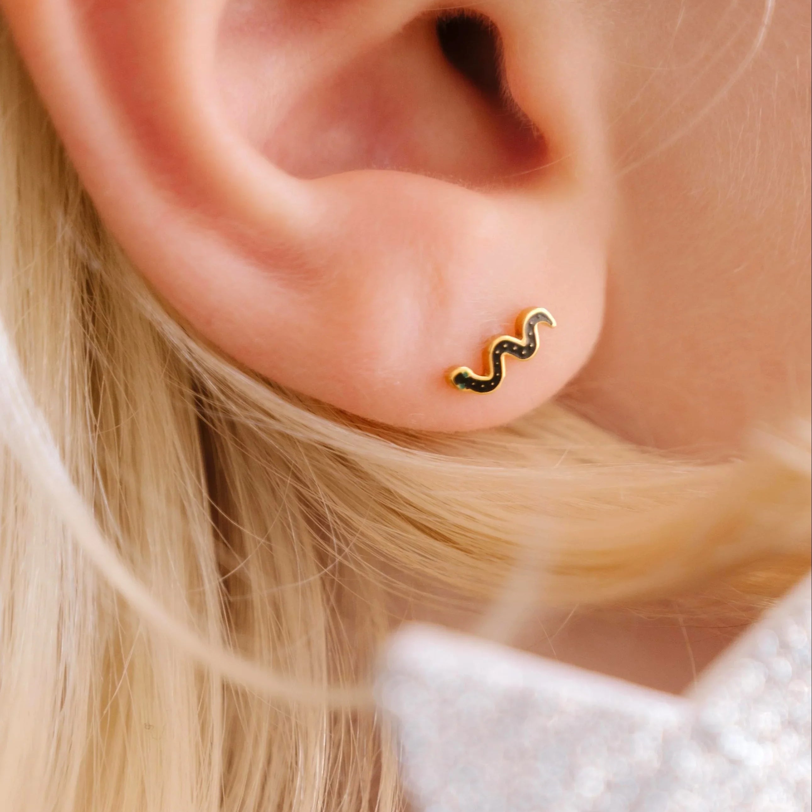 Close-up of a person wearing a gold and black snake earring with a blurred star-shaped object in the foreground.