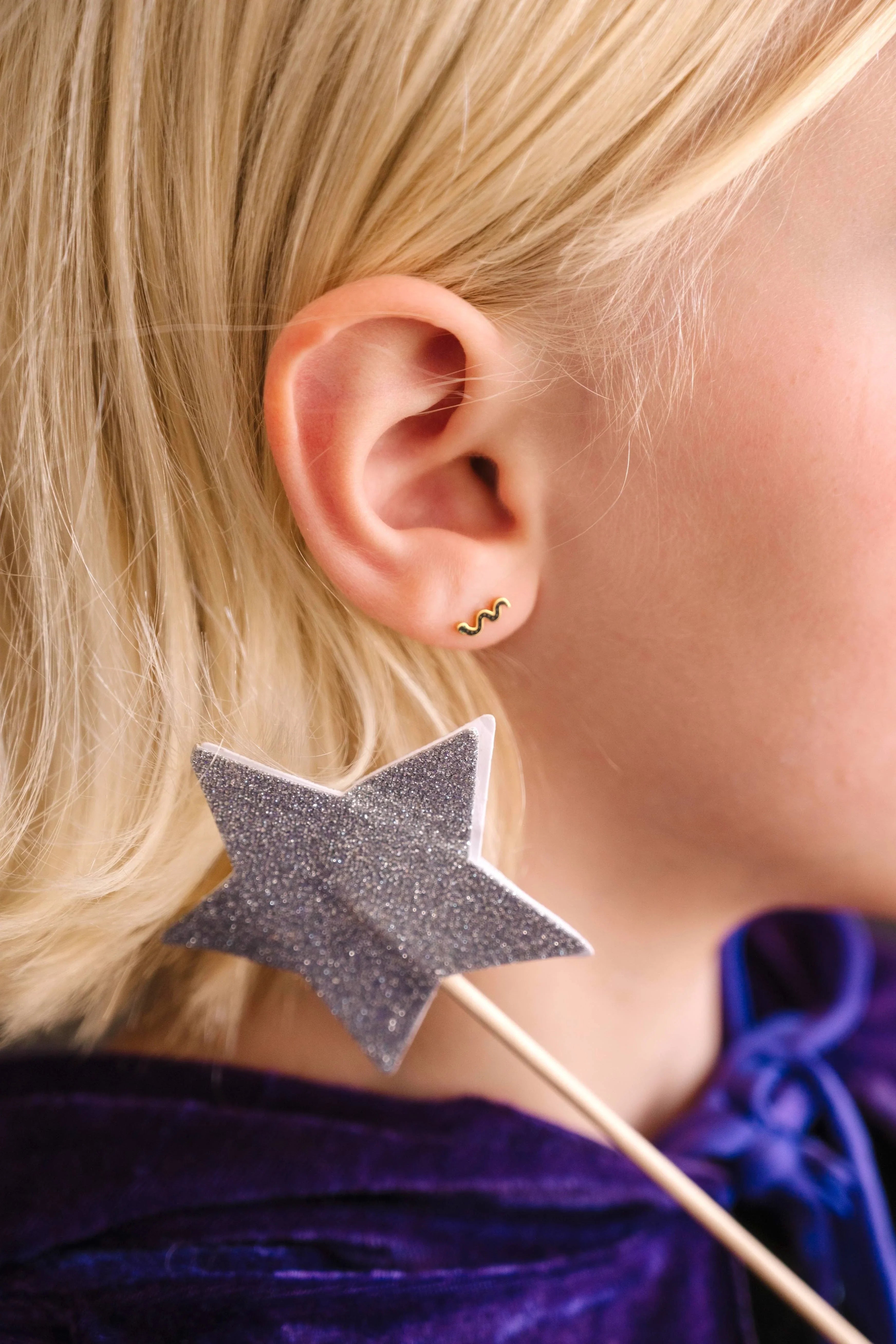 Close-up of a child wearing a black enamel snake-shaped earring with a blurred background