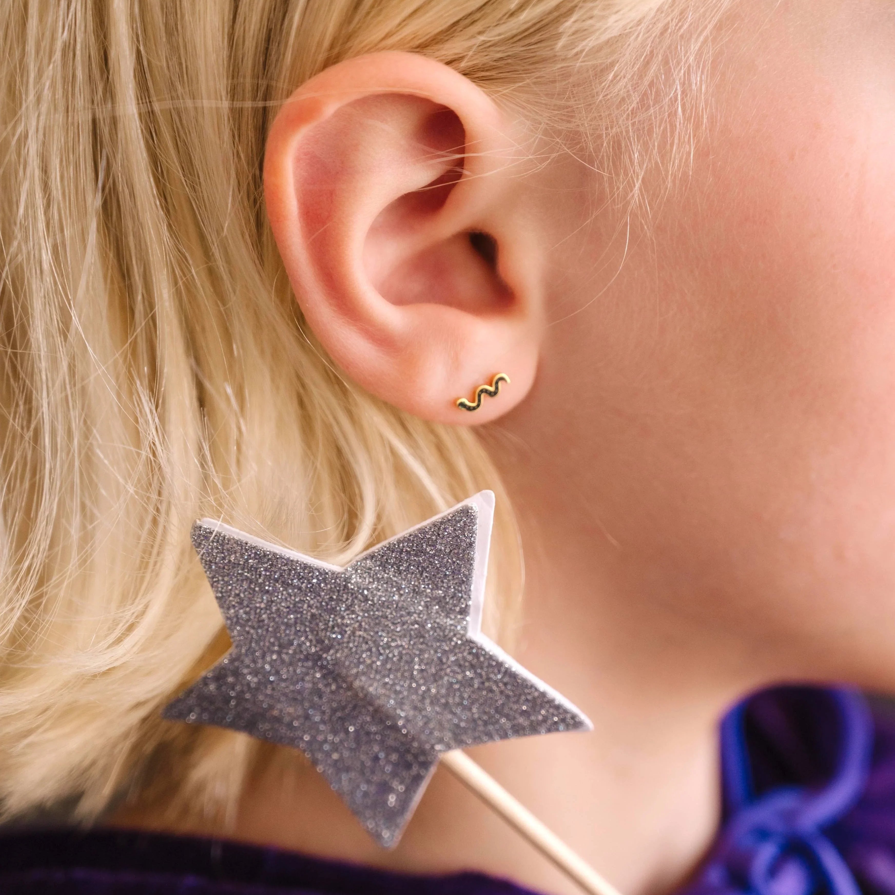 Close-up of a child wearing a black enamel snake-shaped earring with a blurred background