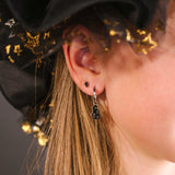 Close-up of an person wearing a black hat with gold star accents and wearing a silver hoop with a black enamel haunted house charm on it.
