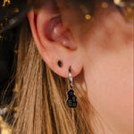 Close-up of an ear wearing a silver hoop with a black enamel haunted house charm on it.