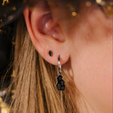 Close-up of an ear wearing a silver hoop with a black enamel haunted house charm on it.