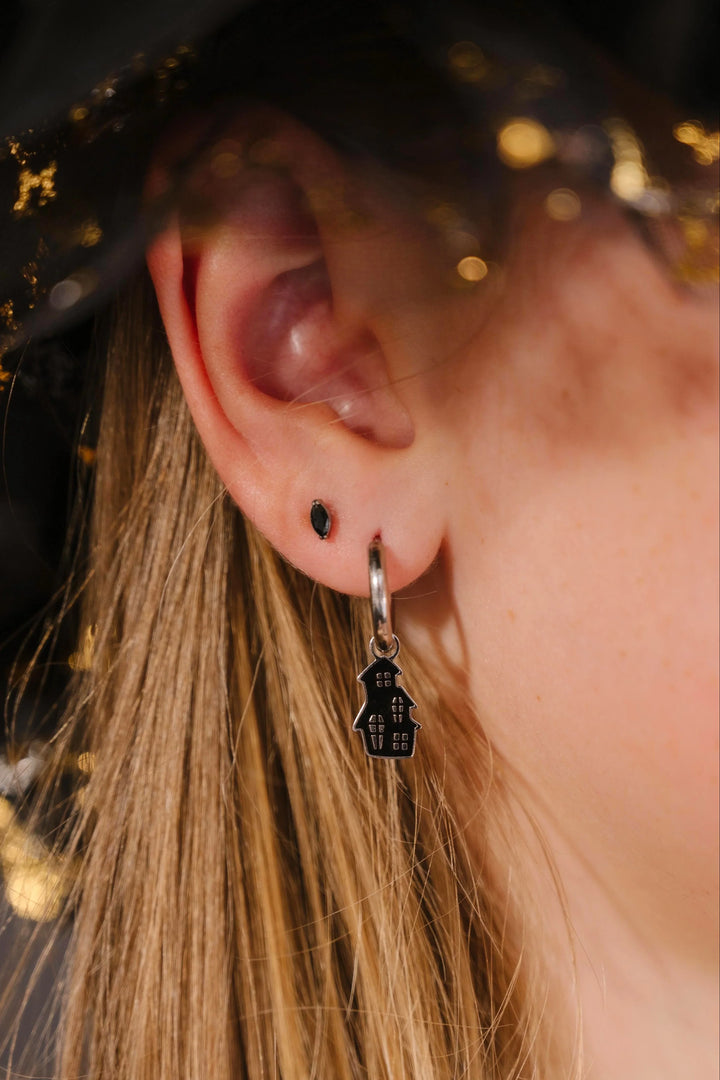 Close-up of an ear wearing a silver hoop with a black enamel haunted house charm on it.