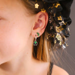Close-up of a person in a black and gold starred witch hat, wearing a silver hoop with a black and green enamel cauldron charm.